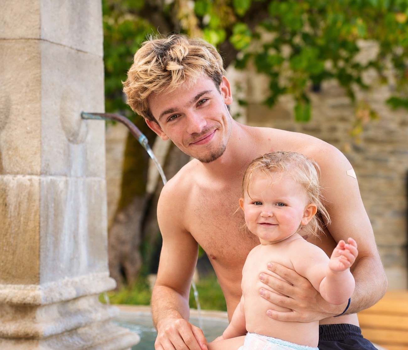 Young man holding a baby by a garden fountain